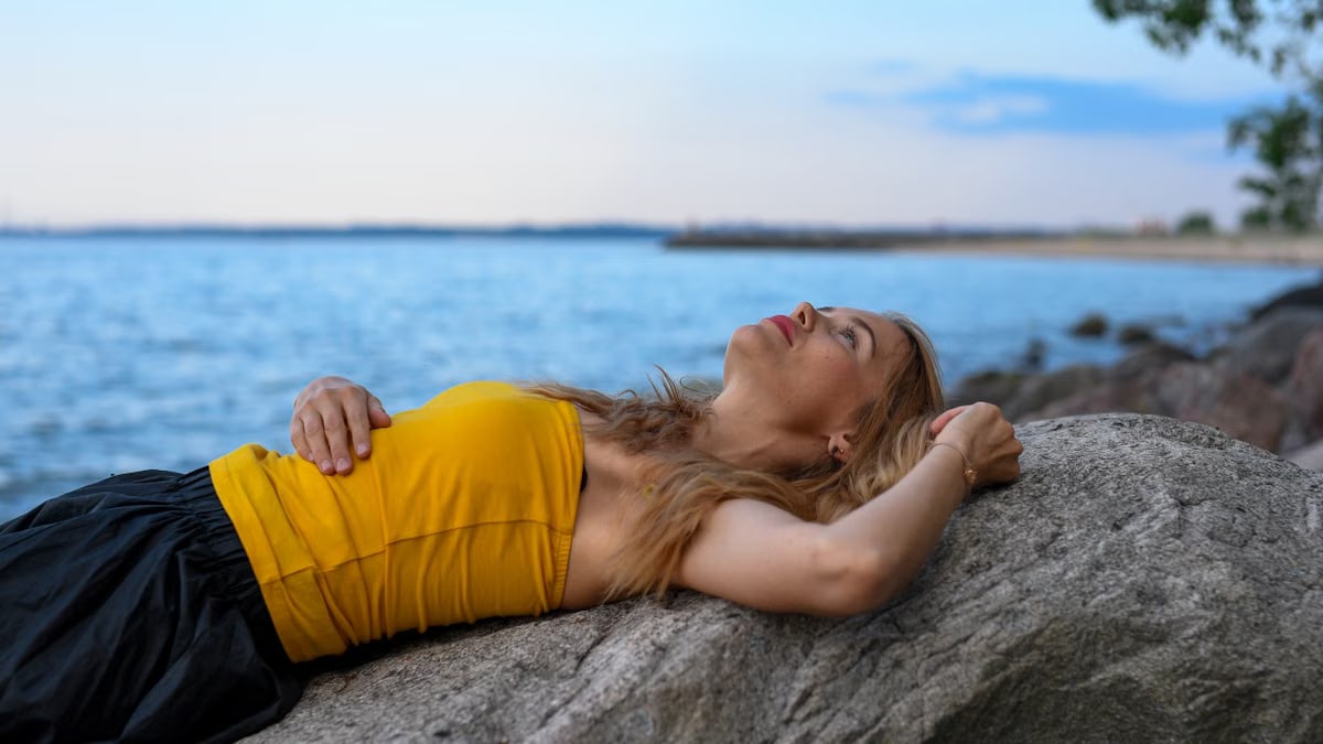 A woman peacefully relaxes on rocks by the sea in Tallinn during a calm summer day.