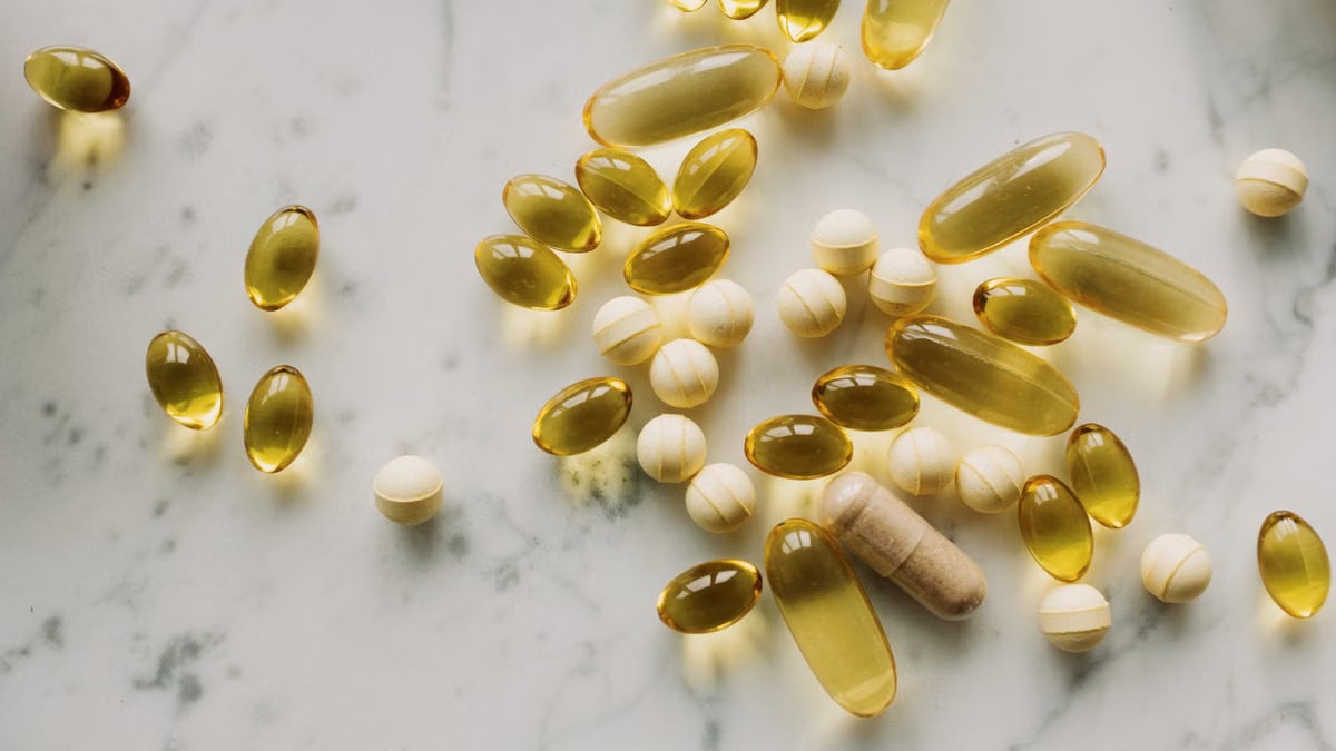 A variety of capsules and pills scattered on a light marble background.
